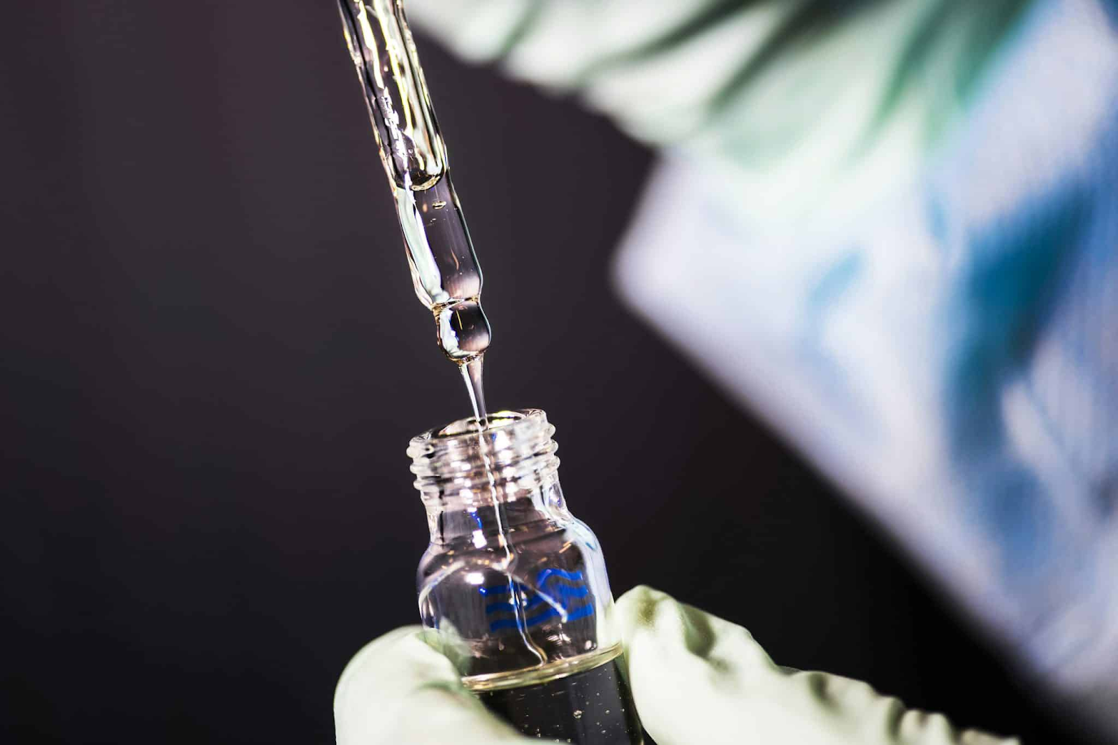 gloved-hand-holding-glass-bottle-while-dropper-dispenses-clear-liquid-against-dark-background-full-spectrum-optimization-how-to-stack-prostamax-and-peptides-for-peak-results-tony-huge