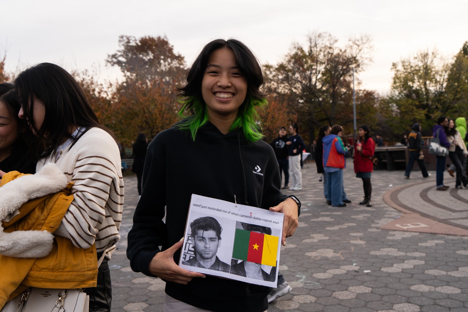 An image of a crowd member at the Zayn Malik look-alike contest holding a sign referencing an X post about Malik’s hair strand.