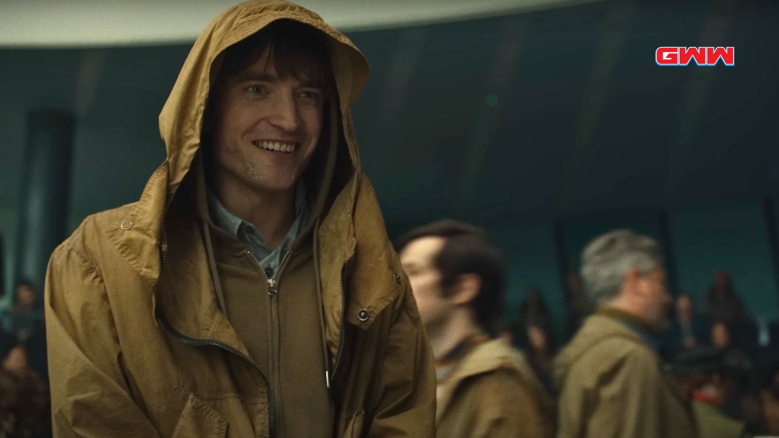 Mickey smiling and wearing a hooded jacket in a crowded environment.