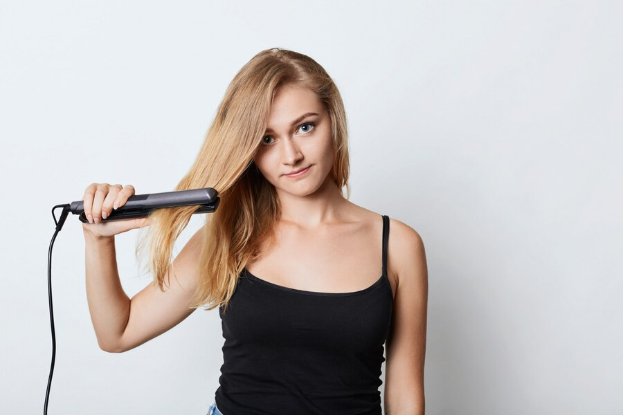 Blonde female in black cloth using hair straightener