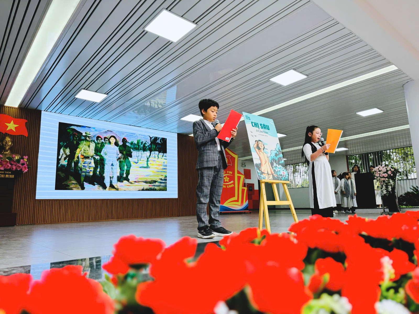 A group of kids standing in a room with red flowers

Description automatically generated