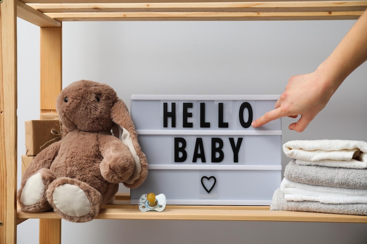 Étagère de chambre de bébé avec peluche, serviettes, tétine et panneau lumineux “Hello Baby”.