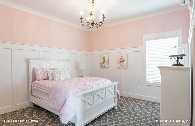 This bedroom features pink and white wainscoted walls, white furnishings, and gray patterned carpet flooring.