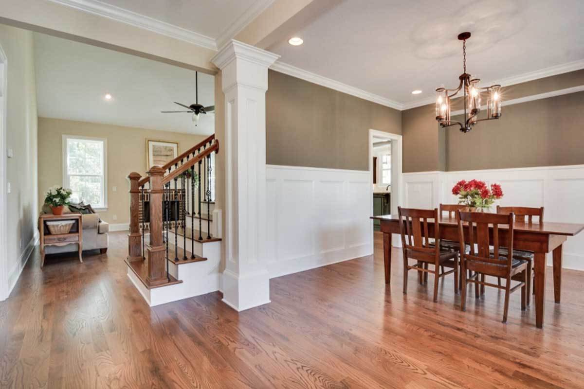 Formal dining room with wainscoted walls, an iron chandelier, and a wooden dining set that blends in with the hardwood flooring.