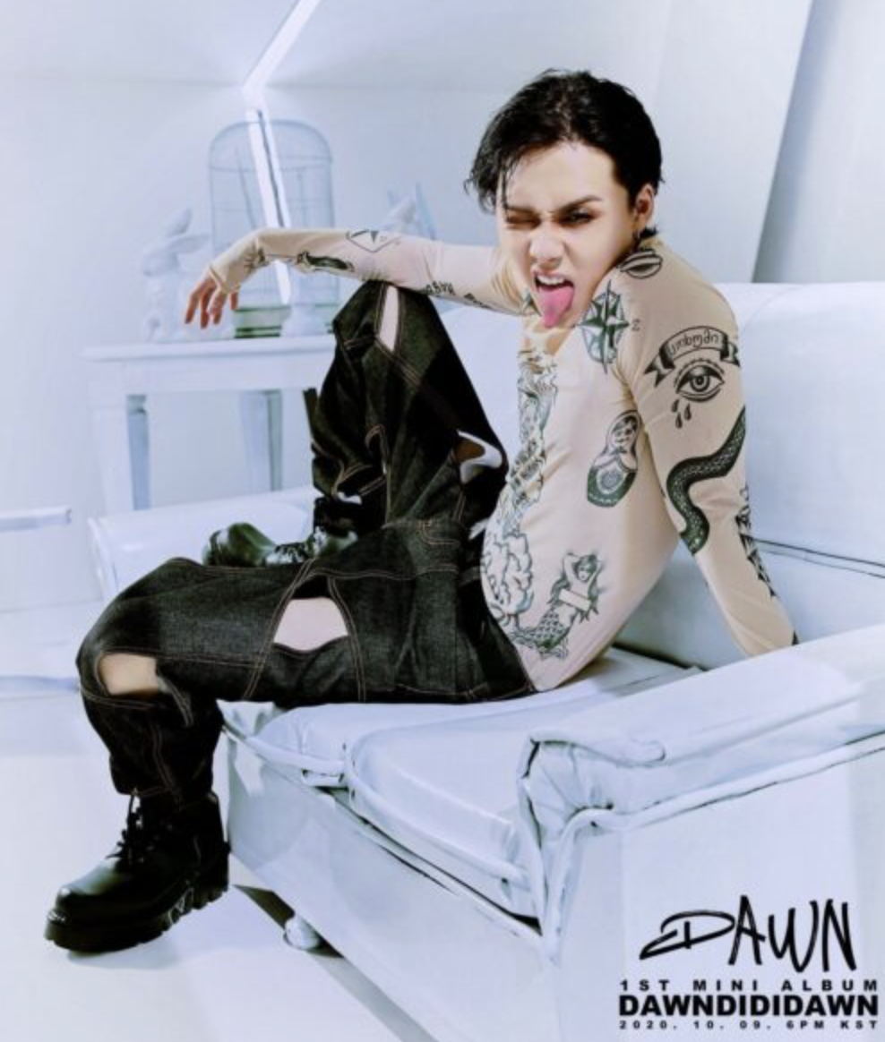 A picture of DAWN recent look sitting on a white chair and making a funny face with his tongue out of his mouth  