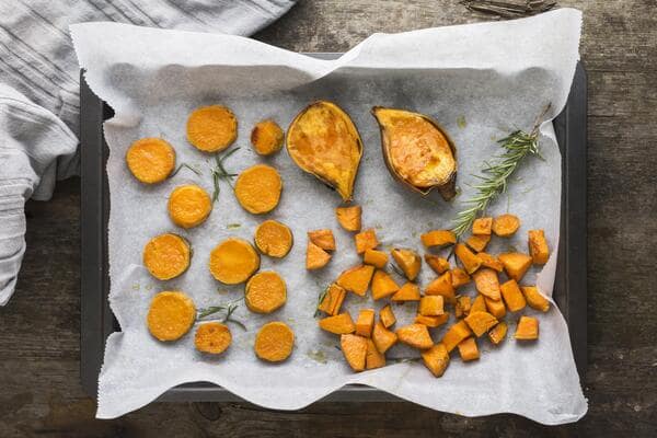 A baking tray lined with parchment paper displaying roasted sweet potato rounds, chunks, and halves