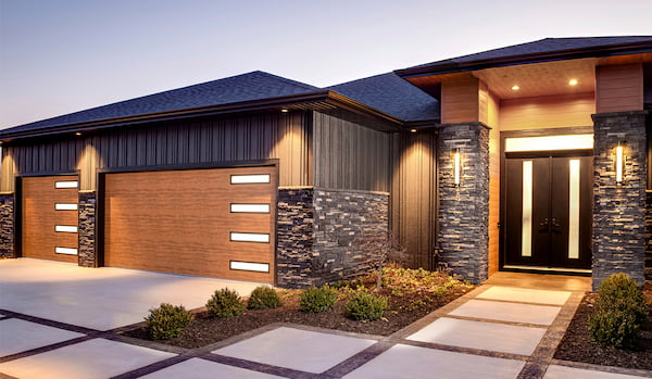 a modern house exterior with a stylish design. The house features a contemporary facade with a combination of materials such as wood, stone, and metal elements. The garage doors are made of wood with horizontal frosted glass panels, adding a sleek and sophisticated look