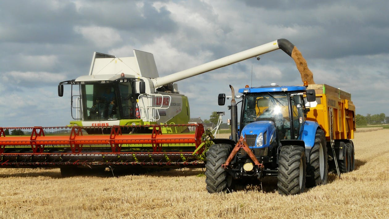 Modern harvester reaping a golden wheat field while unloading grain into a blue tractor trailer, showcasing advanced farming technology.