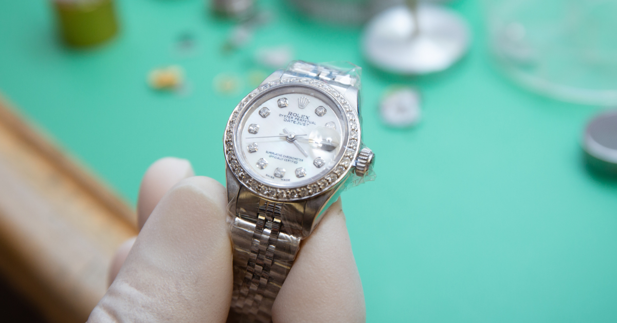 A watchmaker holding a silver Rolex for repair or maintenance.