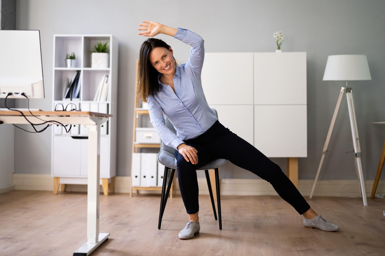 An office worker stretching at her desk to combat the effects of static loading ergonomics.