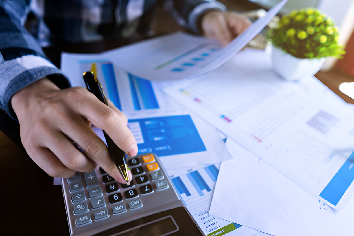 Person using a calculator and analyzing financial charts for bookkeeping and tax preparation.