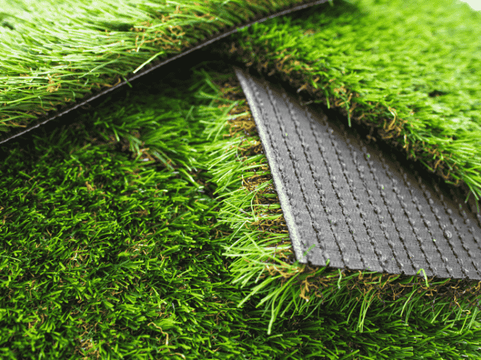 Close-up view of stacked artificial grass carpet rolls showing the green synthetic turf blades and the black perforated backing layer.