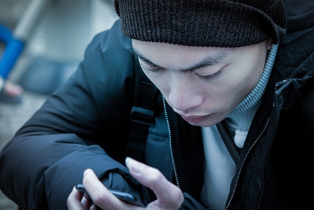 A teen's social media addiction is shown by a man on a mobile phone in the cold