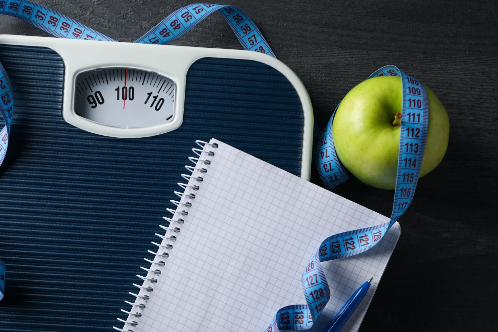 bmi calculator idea being showcased with weight machine, apple, and measuring tape.