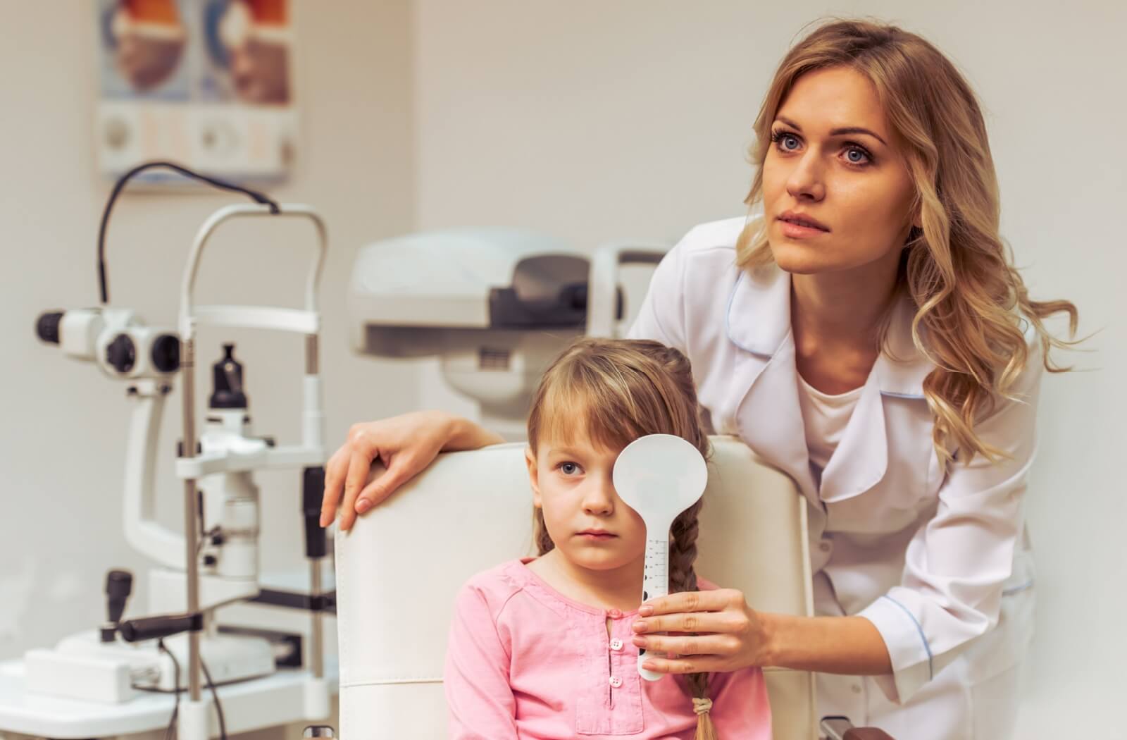 An optometrist helps cover their young patients' eye during a visual acuity test.