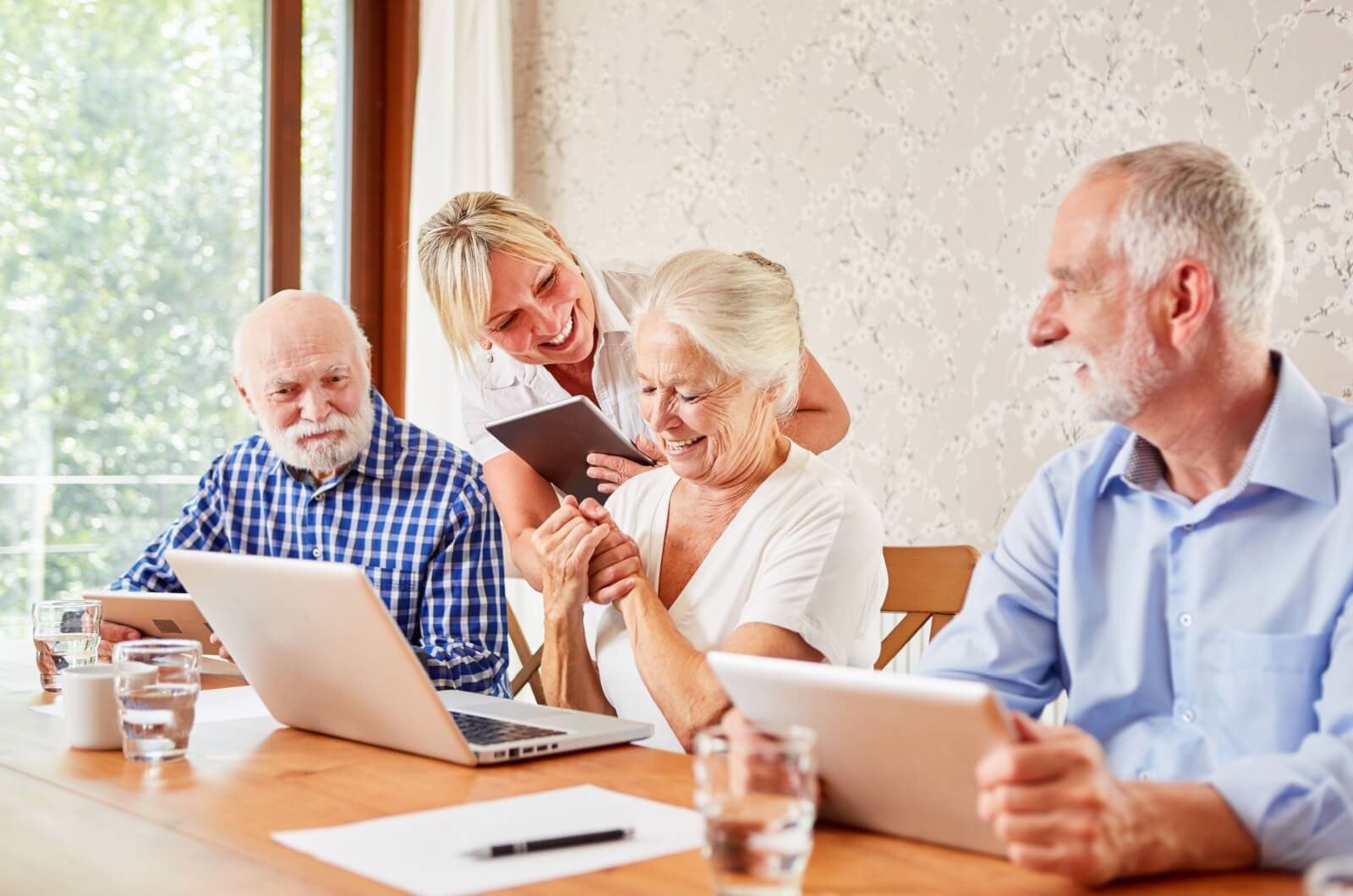 A group of older adults in senior living sitting at a table with laptops during a computer class led by an instructor.