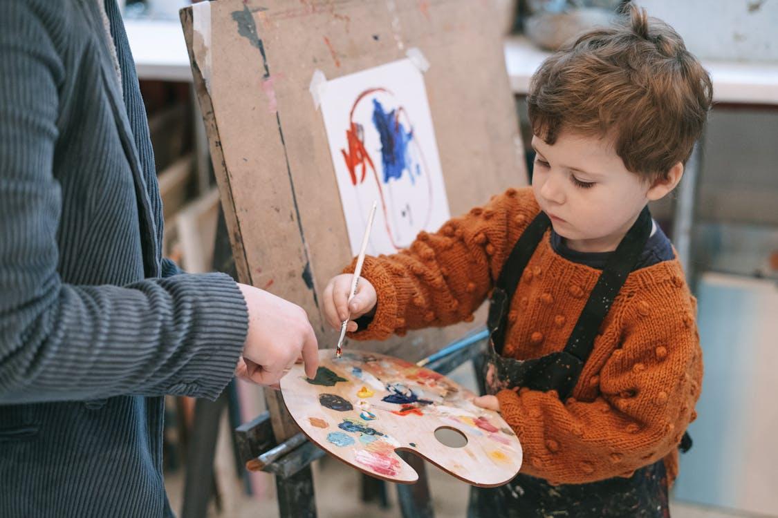 Free Young boy learning to paint with teacher's guidance during art class. Stock Photo