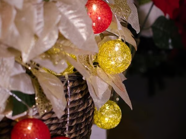 Cesta decorada com folhas claras e bolas de Natal vermelhas e amarelas com lâmpadas em seu interior.