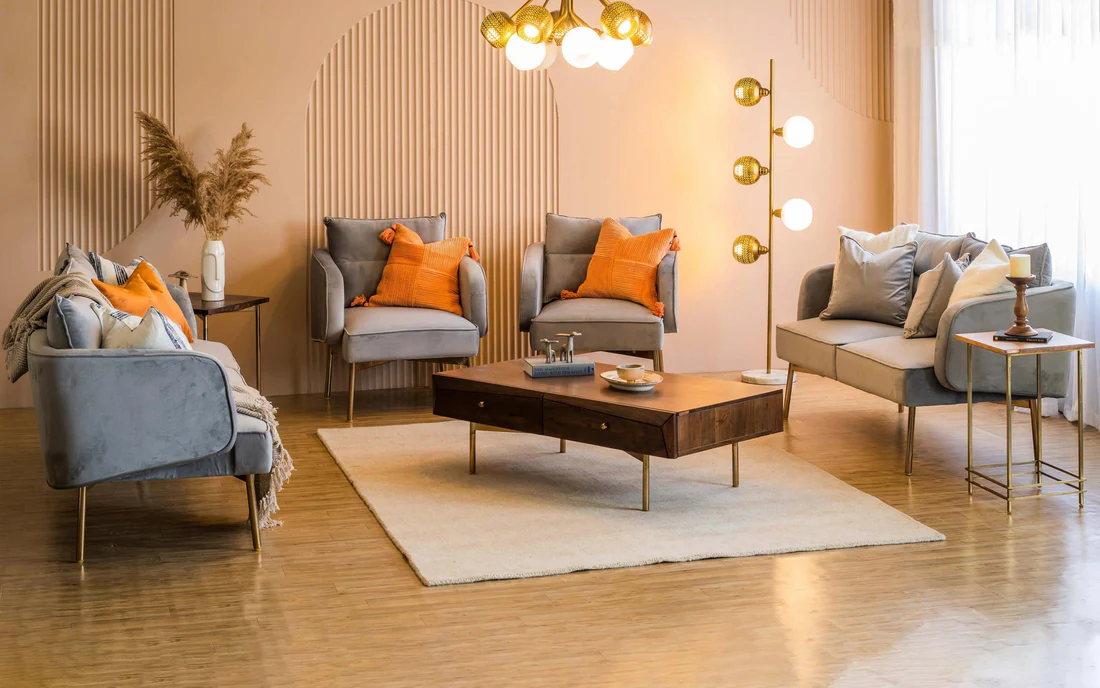 Modern living room with grey velvet sofas and chairs accented with orange cushions, a solid wood coffee table on a cream rug