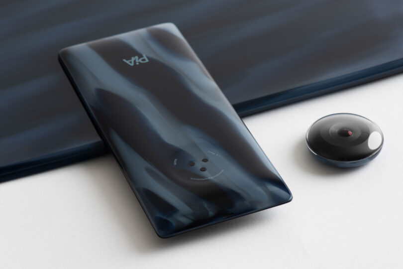 A sleek smartphone with a reflective dark surface is next to a small, spherical camera on a white surface.
