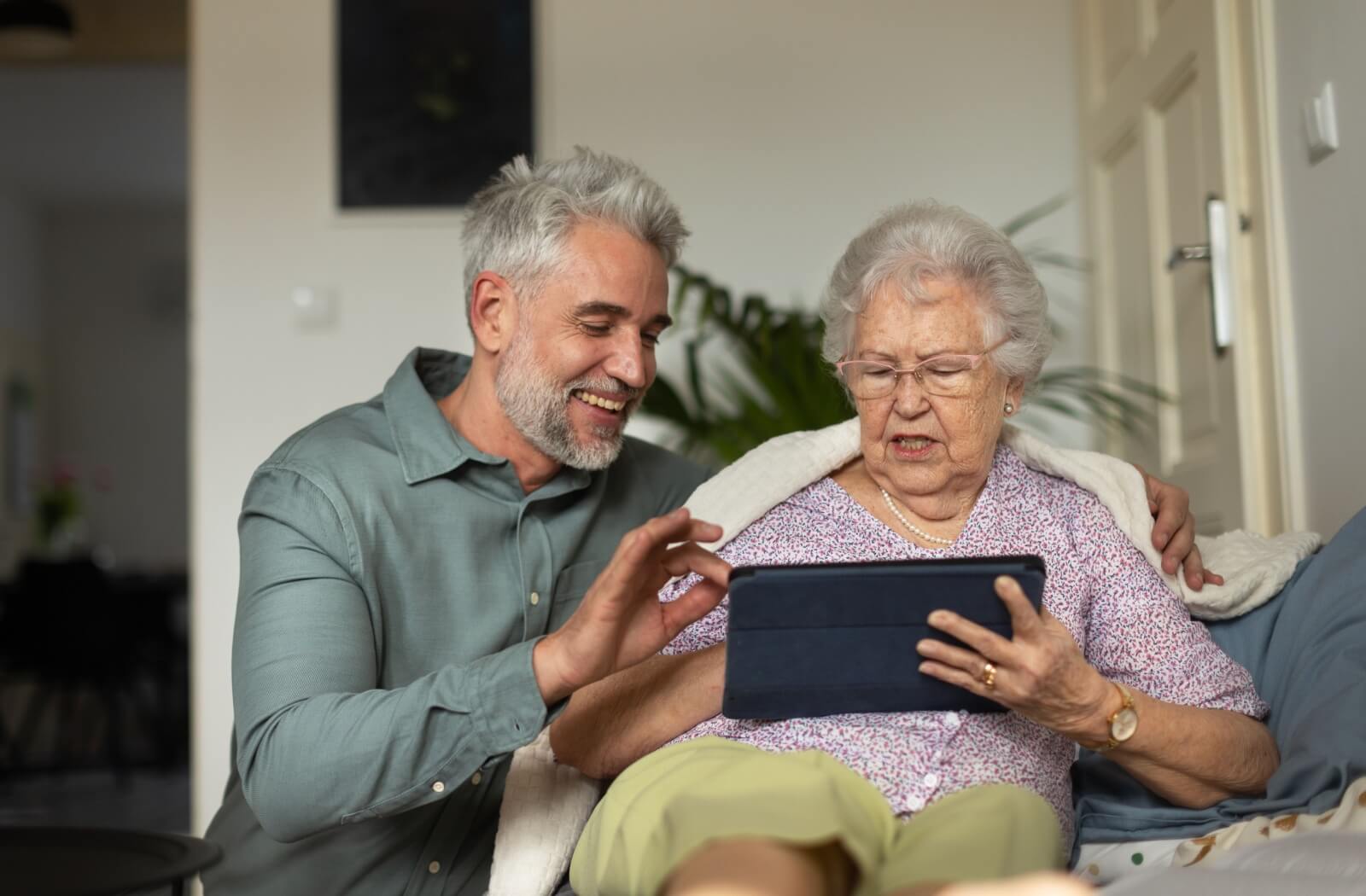 An adult helps their senior parent download an audiobook on their tablet.
