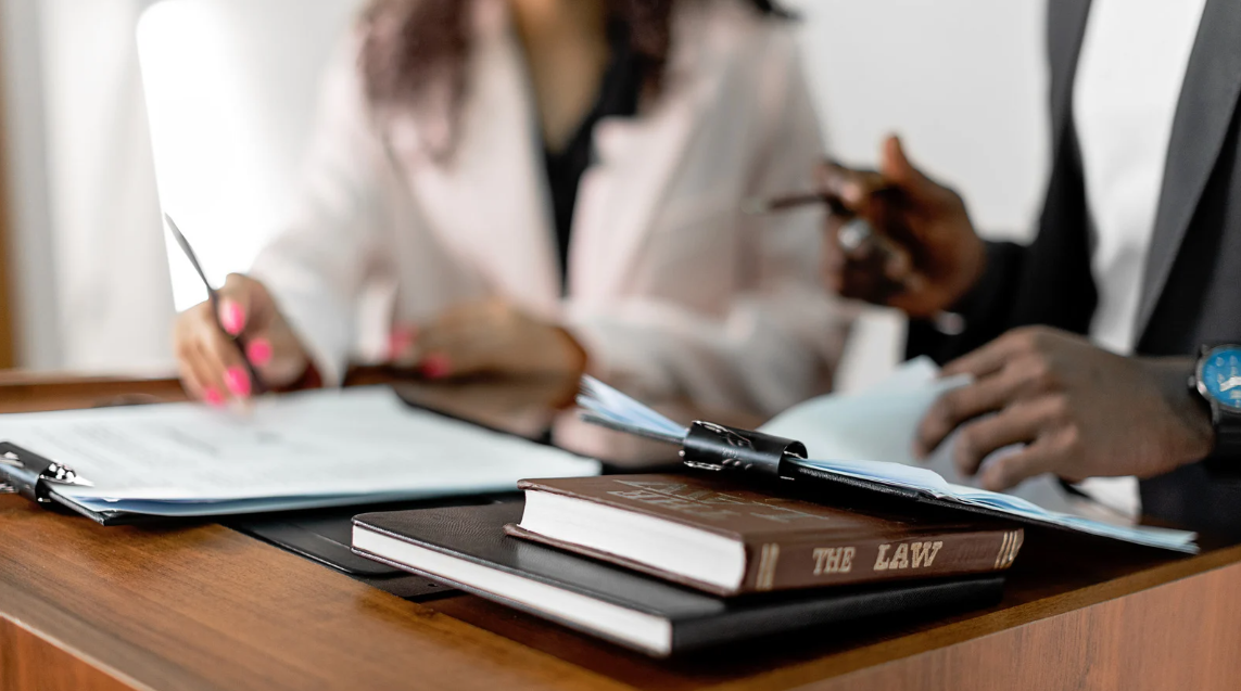 (Close-up of two legal professionals reviewing case documents at a desk, with a law book in focus—symbolizing precision, collaboration, and expertise in legal practice.)