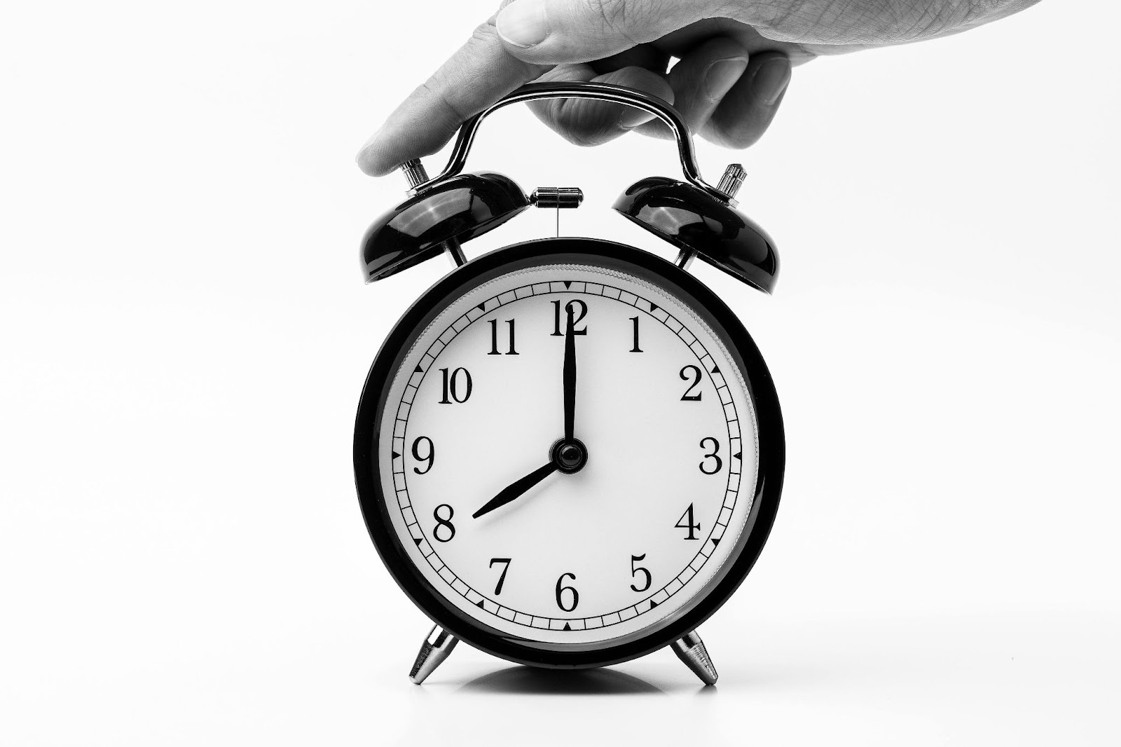 Hand adjusting a black alarm clock with white background.