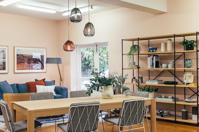 A modern dining room aligned with Vastu principles with a wooden table and six gray chairs, illuminated by three pendant lights.