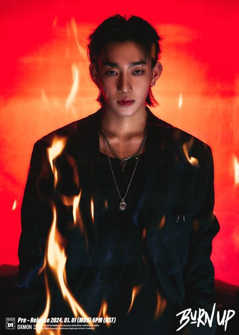 This contain an image of DXMON member Minjae with long hair wearing a black jacket and flames around his neck, standing in front of a red background