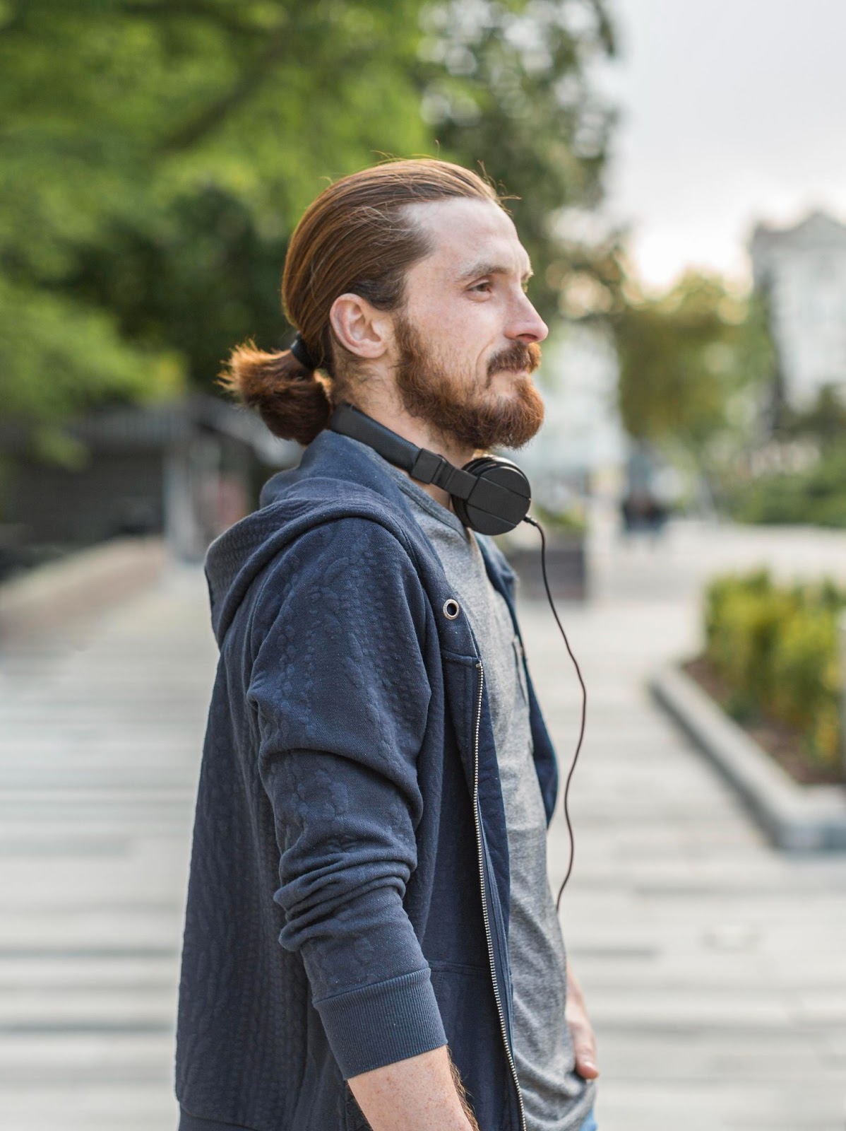 Um homem é visto de perfil usando um rabo de cavalo e fones de ouvido no pescoço.