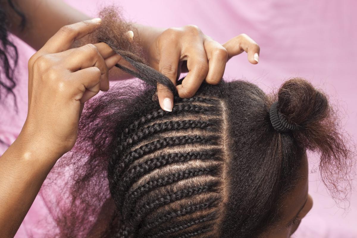 A picture of a woman doing cornrows on a little girl's hair. 