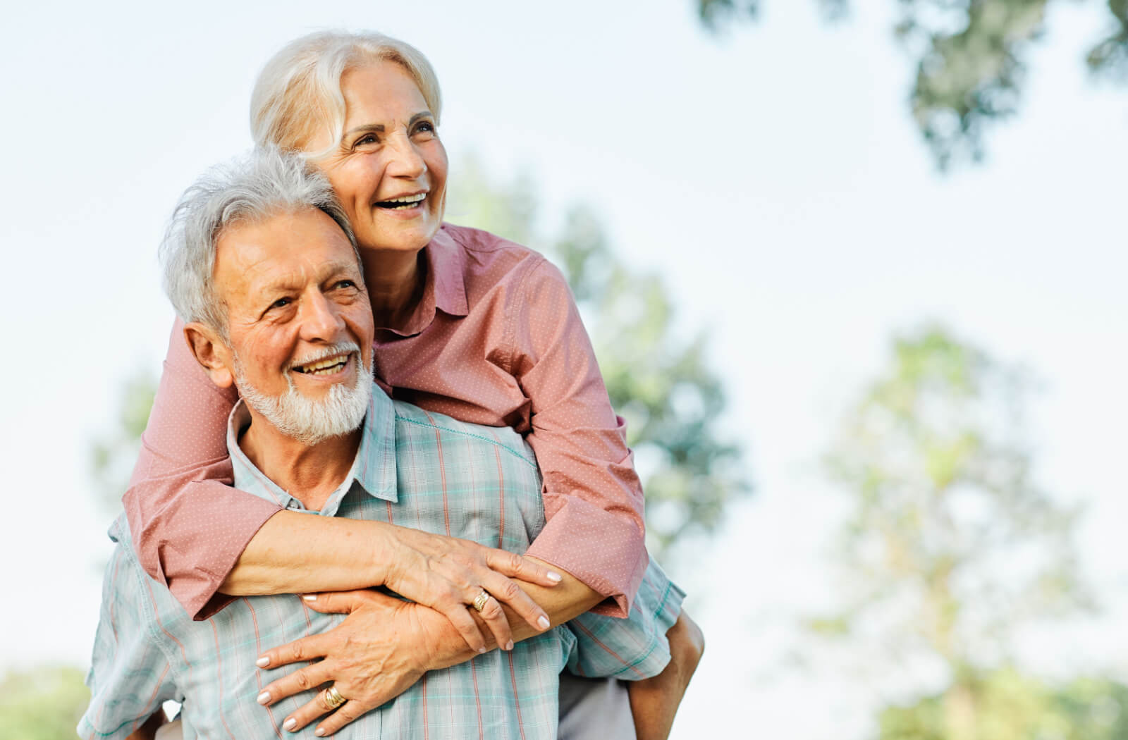 A senior man giving his wife a piggyback and laughing while on a guided tour of a Nashville park.