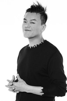 This contain J.Y. Park a black and white photo of a man with his hands folded in front of him