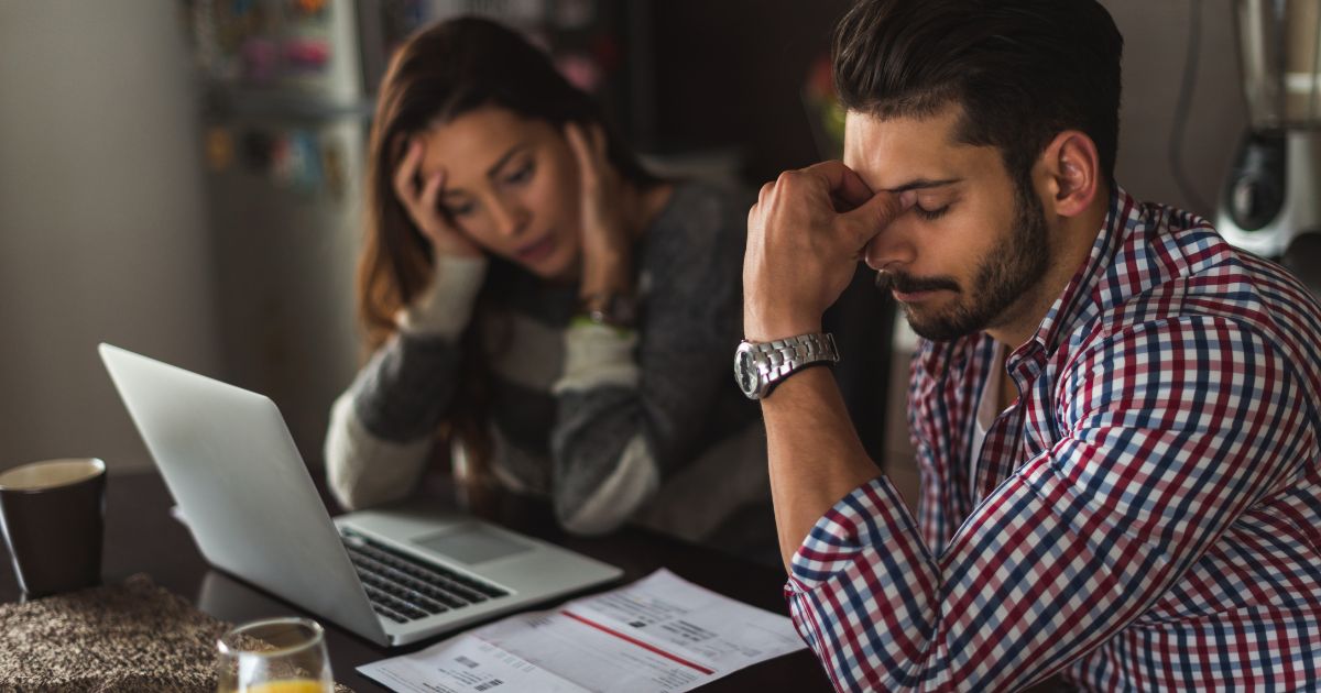 A man and a woman sitting at a table, appearing stressed as they review financial documents and work on a laptop, symbolizing financial or visa-related difficulties.