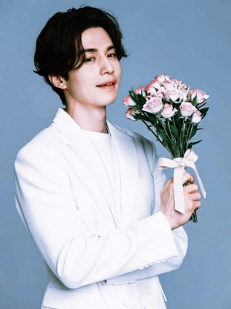 This contains an image of Lee Dong Wook in a white suit holding a bouquet of flowers and looking at the camera