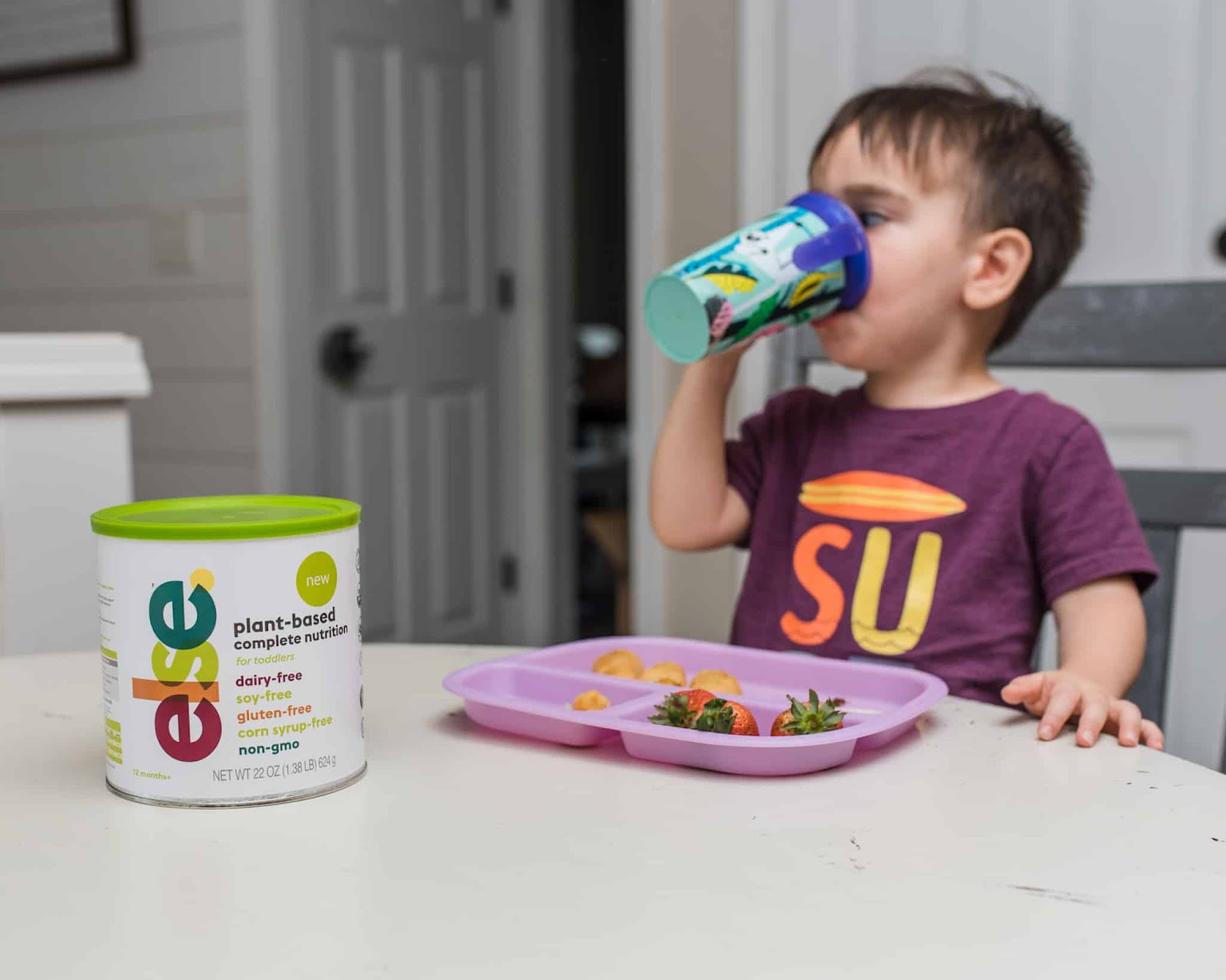 A young boy sits at a table, drinking from a cup with a focused expression.