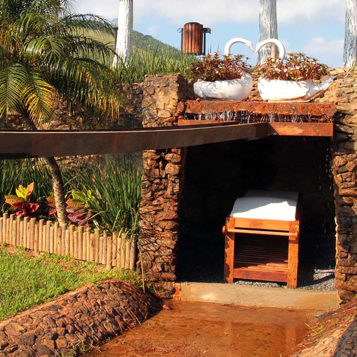 spa ao ar livre com estrutura de pedra, cercada por plantas e flores em vasos brancos.