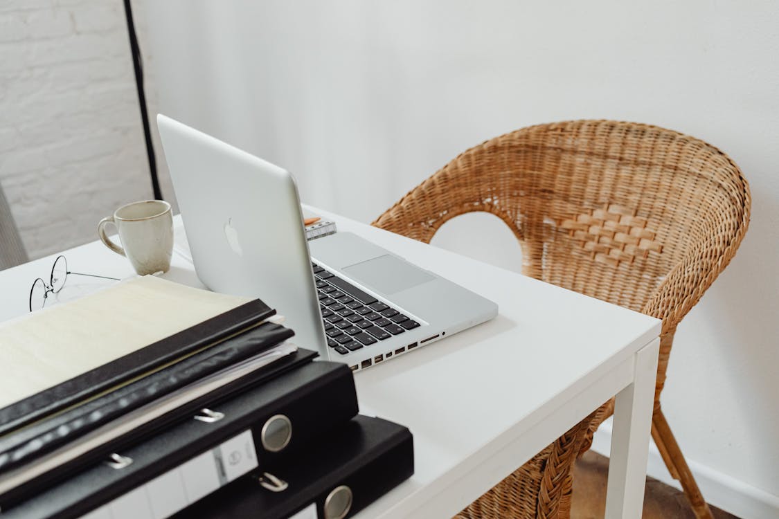 Free A cozy home office setup featuring a laptop, binders, and wicker chair for productive remote work. Stock Photo