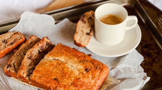 Pain aux bananes protéiné tranché sur une plaque de cuisson avec une tasse de café, prêt à être servi.