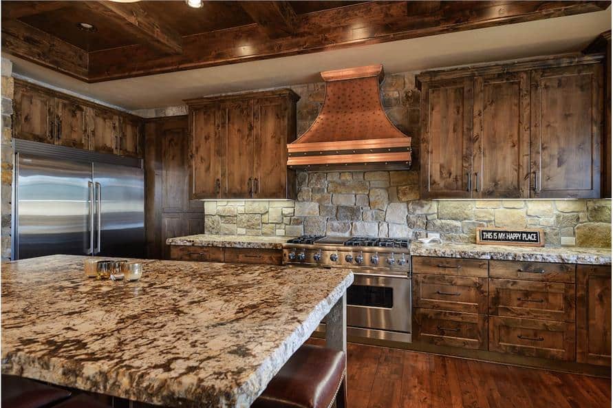 The kitchen includes stainless steel appliances and a copper vent hood fixed against the stone backsplash.