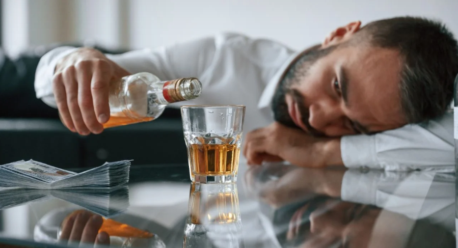 A person sleeping at a table with a glass of alcohol

Description automatically generated