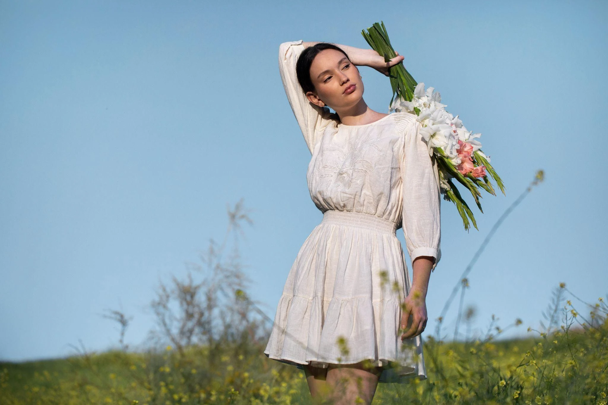 cottage-core girl in white dress holding flowers in a field