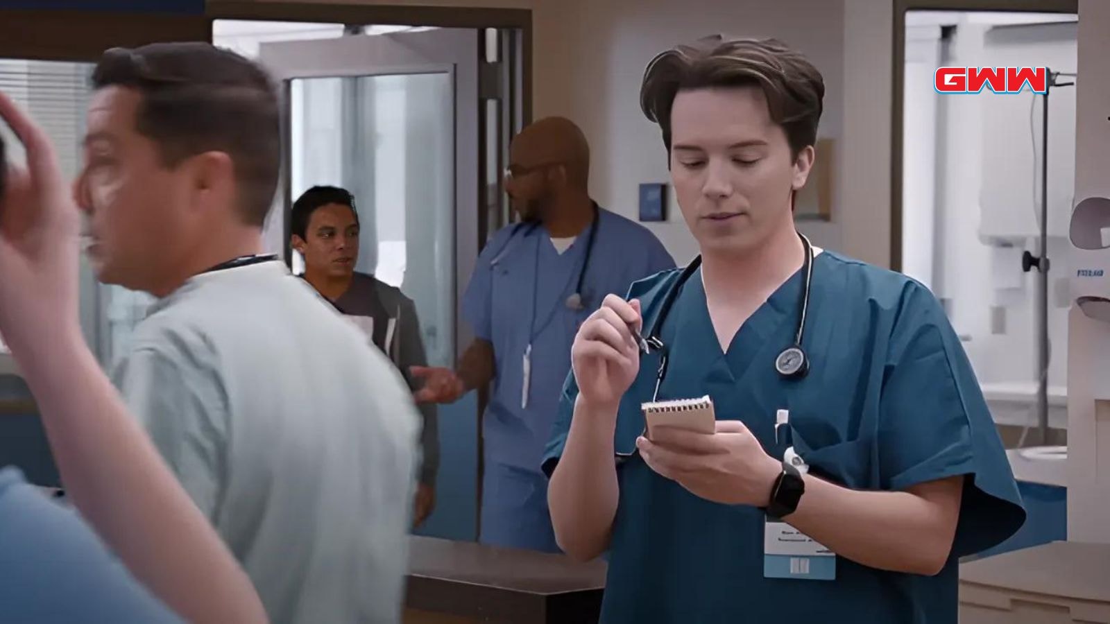 Josh Lawson writes on a notepad in a bustling hospital setting