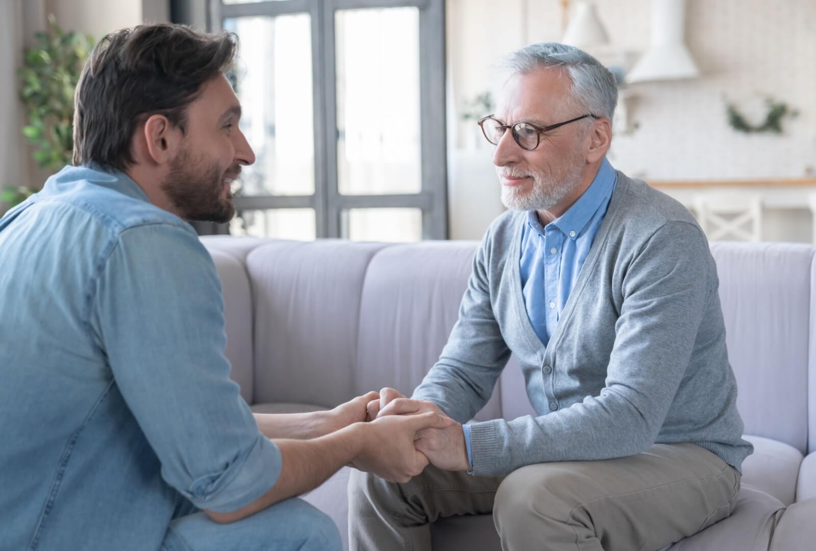 An adult son sitting with his elderly father checking in on his wellbeing and happiness.