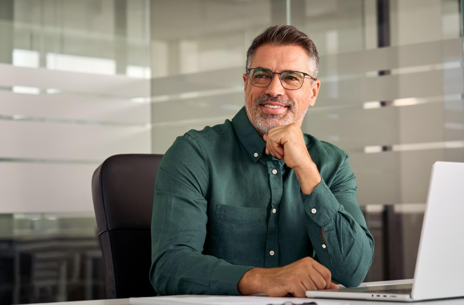 A smiling office worker taking a screen break by looking away from their laptop.