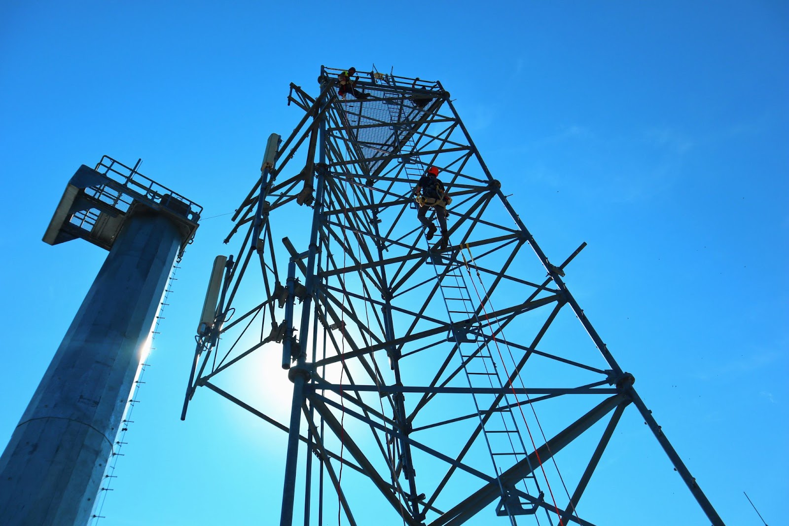 Pinnacle Career Institute outdoor climbing lab we see a tower technician student climbing a tower against a blue sky