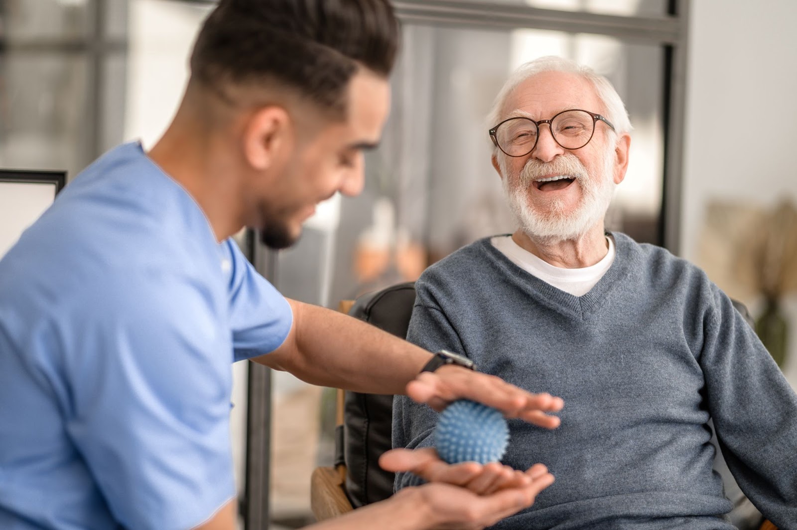 Senior man laughing while receiving physical therapy with a stress ball.