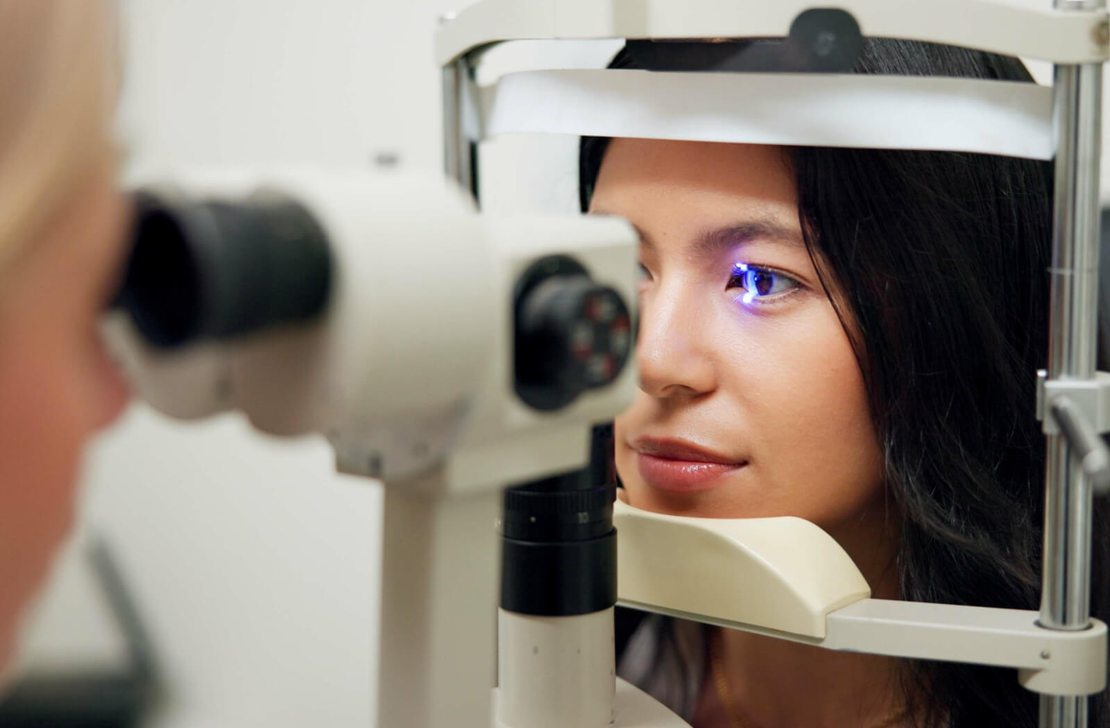 A patient smiling while her optometrist performs a slit-lamp test during her comprehensive eye exam.