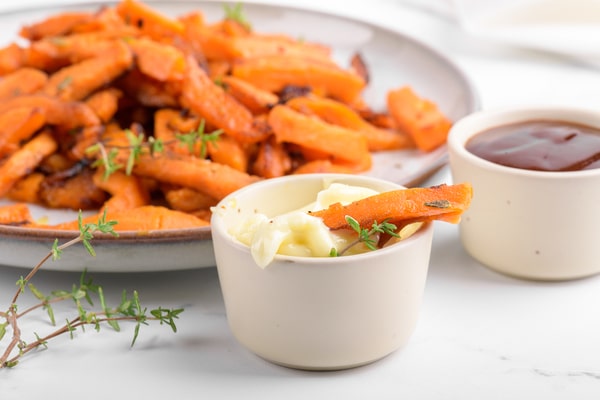 Air-fried sweet potato fries served with creamy mayonnaise and barbecue dipping sauces, garnished with fresh thyme on a white table