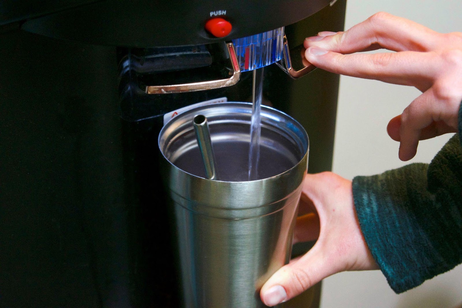 hands holding a cup being filled at a water station